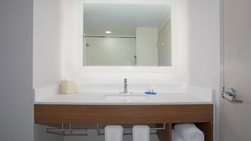 Uma casa de banho com uma pia branca, um espelho, um porta-toalhas e um toucador de madeira.