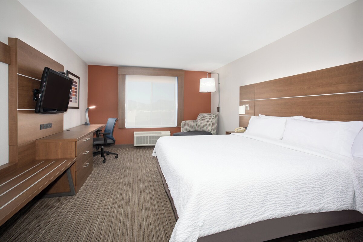 Hotelkamer met een bed, een bureau met stoel, een televisie, een raam en een lamp.