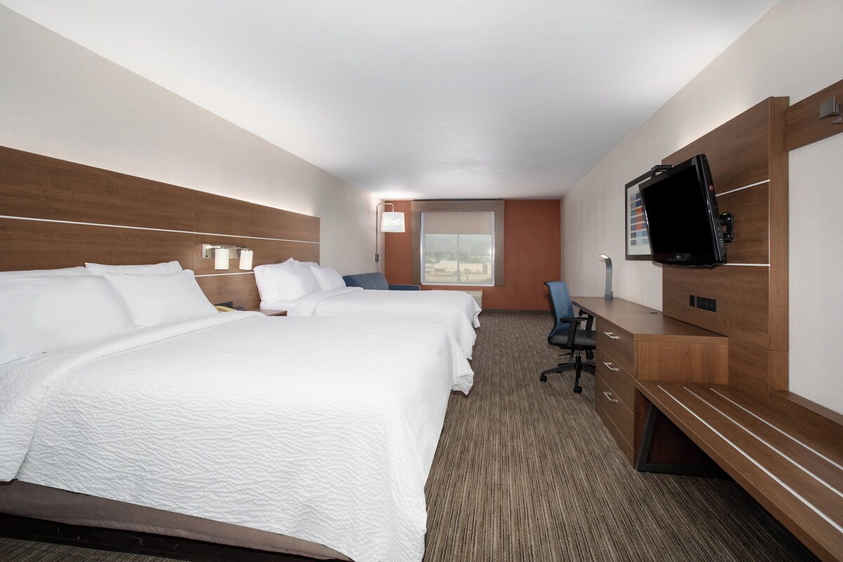 Een hotelkamer met twee bedden, een bureau, een stoel, een televisie en een raam.