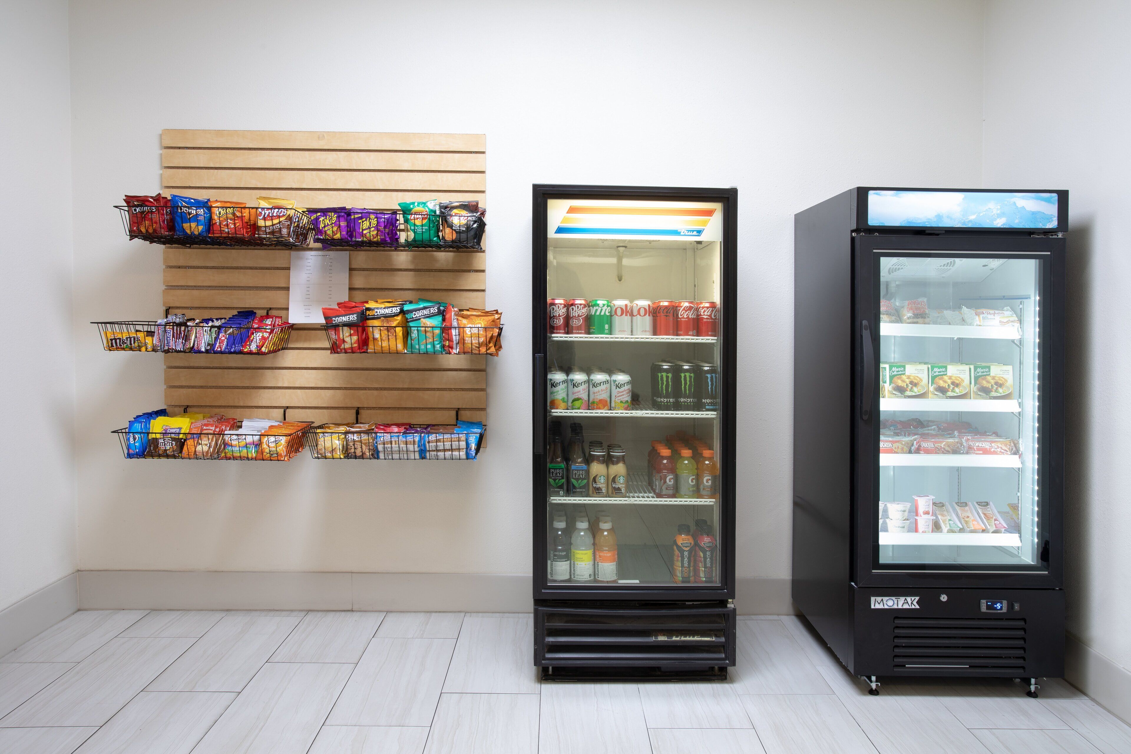 A vending machine with snacks and drinks, a refrigerated display case, and a wooden wall with snack bins.