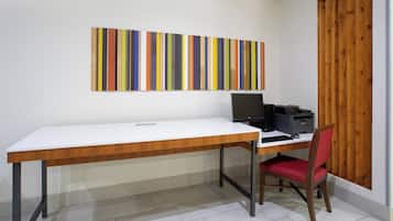 Un espacio de trabajo con un escritorio blanco, una silla roja, una computadora e impresora. Un colorido cuadro a rayas cuelga en la pared.