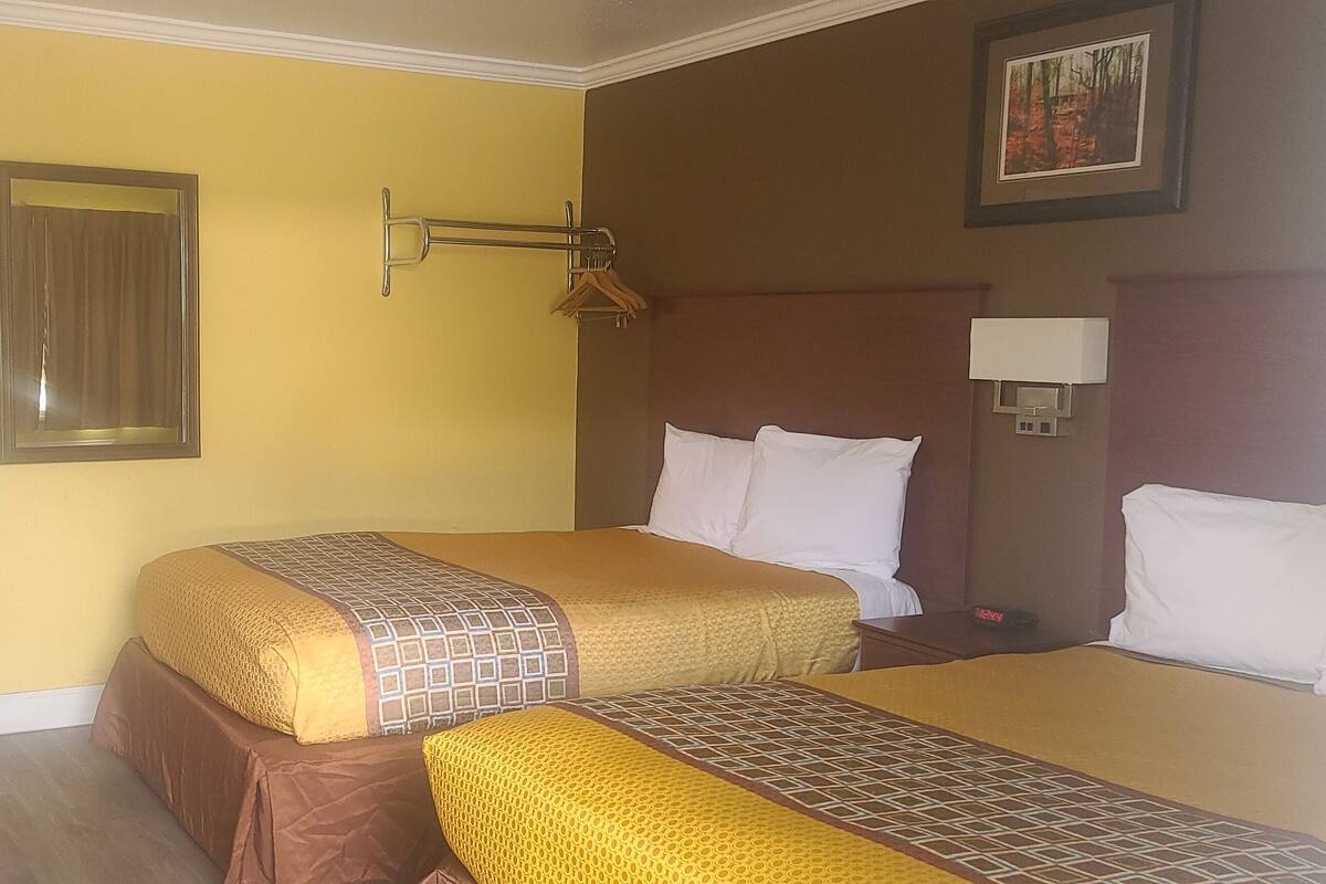 A hotel room with two beds, a desk, a mirror, a wall-mounted lamp, and a framed picture.