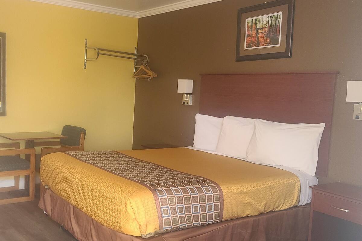 A hotel room with a bed, a desk, a chair, a bedside table, and a wardrobe.