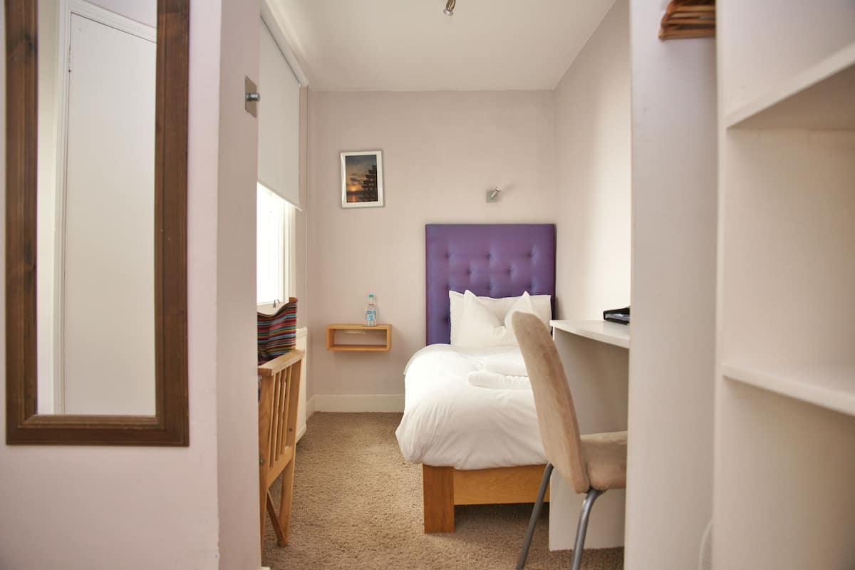 Een slaapkamer met een bed, een stoel, een nachtkastje en een plank.