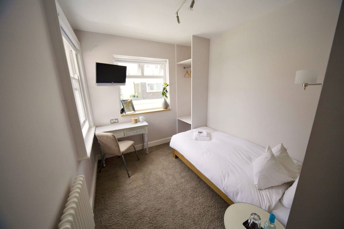 Een kleine, verzorgde kamer met een bed, een bureau en een televisie aan de muur.