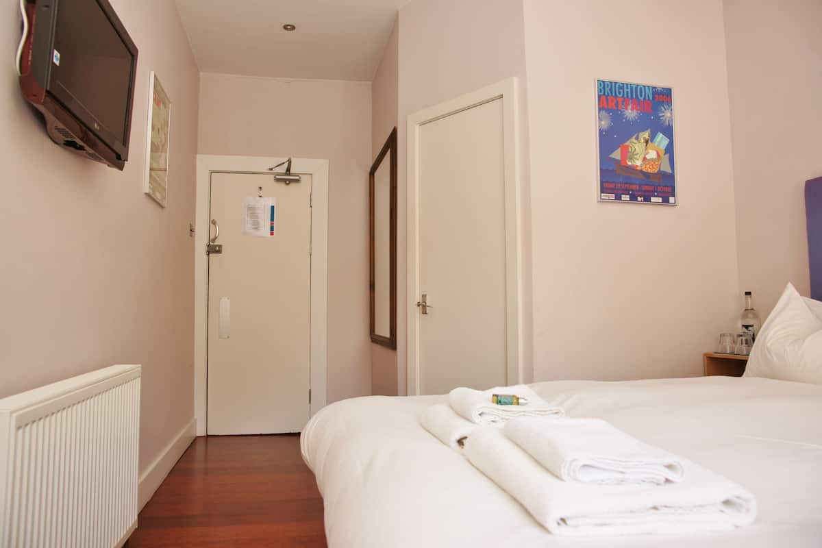 Een hotelkamer met een bed, een deur, een poster aan de muur en een radiator.