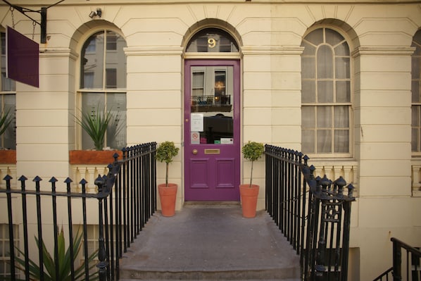 A building with a purple door, numbered 9, and a black iron railing in front.