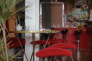 A bar area with red bar stools, a small table with a teapot, and a shelf with various bottles.