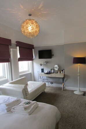 A hotel room with two beds, a desk with a mirror, a television, and a chandelier.