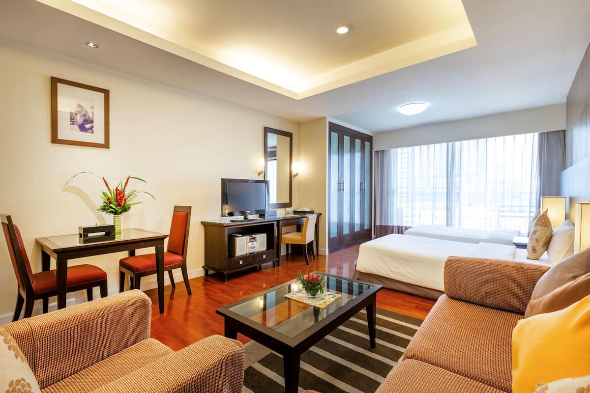 A hotel room with a bed, a sofa, a coffee table, a desk with a chair, a television, and a large window.