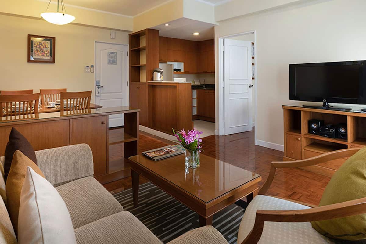 A living room with a sofa, coffee table, and TV. There is a kitchen area with cabinets and a door.
