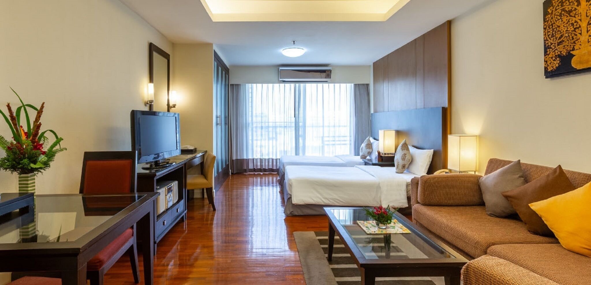 A hotel room with a bed, a sofa, a TV, a desk, and a large window.