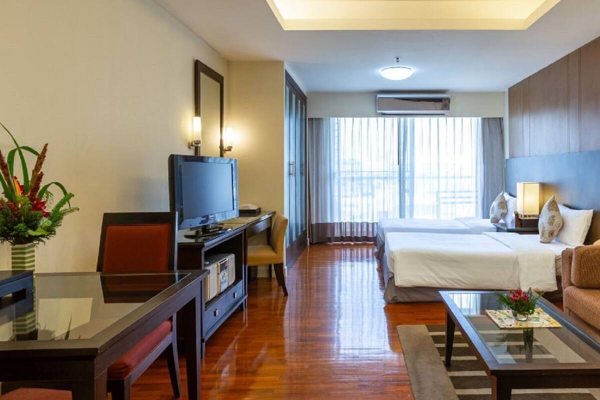 A hotel room with a bed, a sofa, a TV, a desk, and a large window.