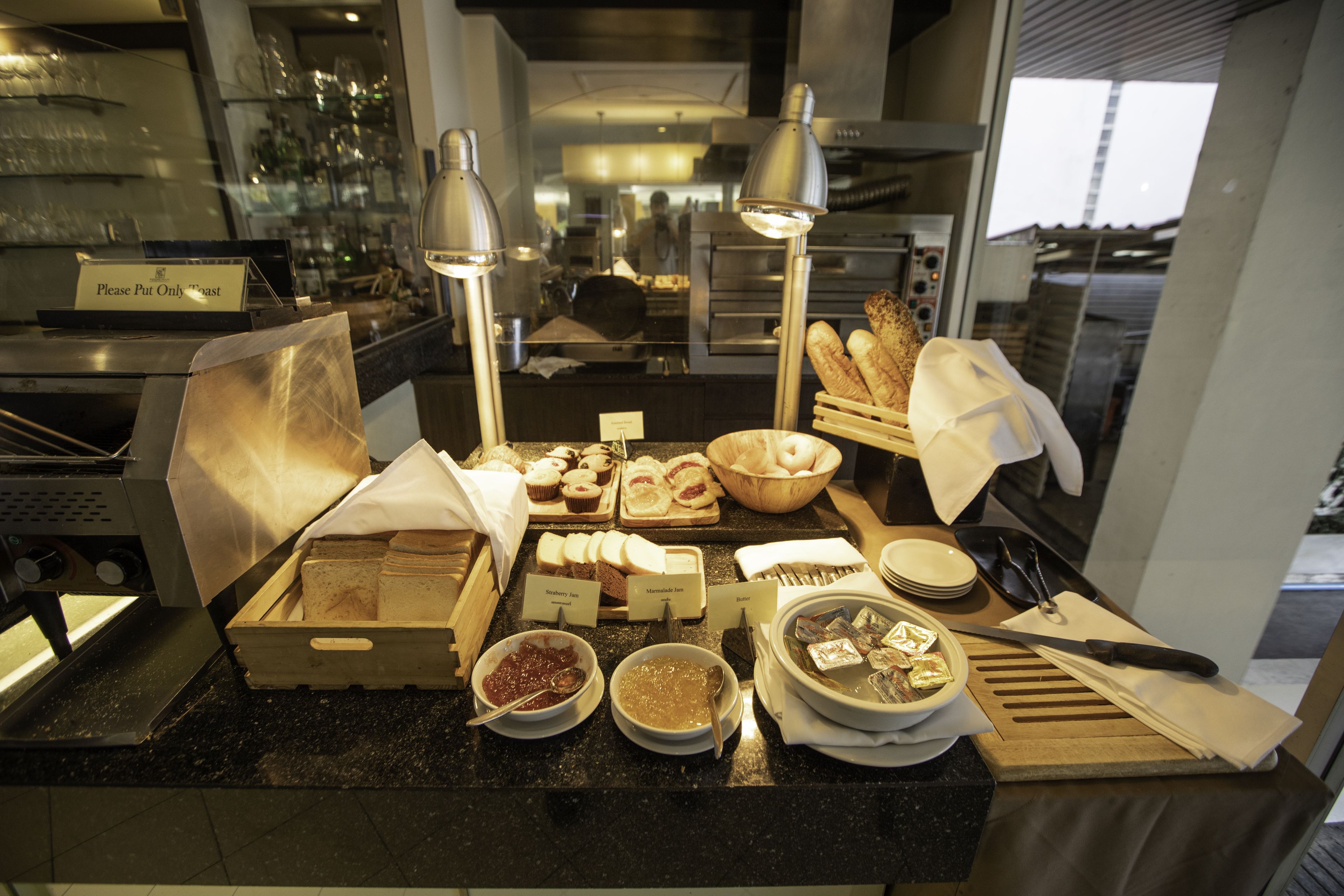 A buffet setup with various food items, including bread, pastries, and condiments, arranged on a counter with a sign indicating 'Please Put Only Toast'.