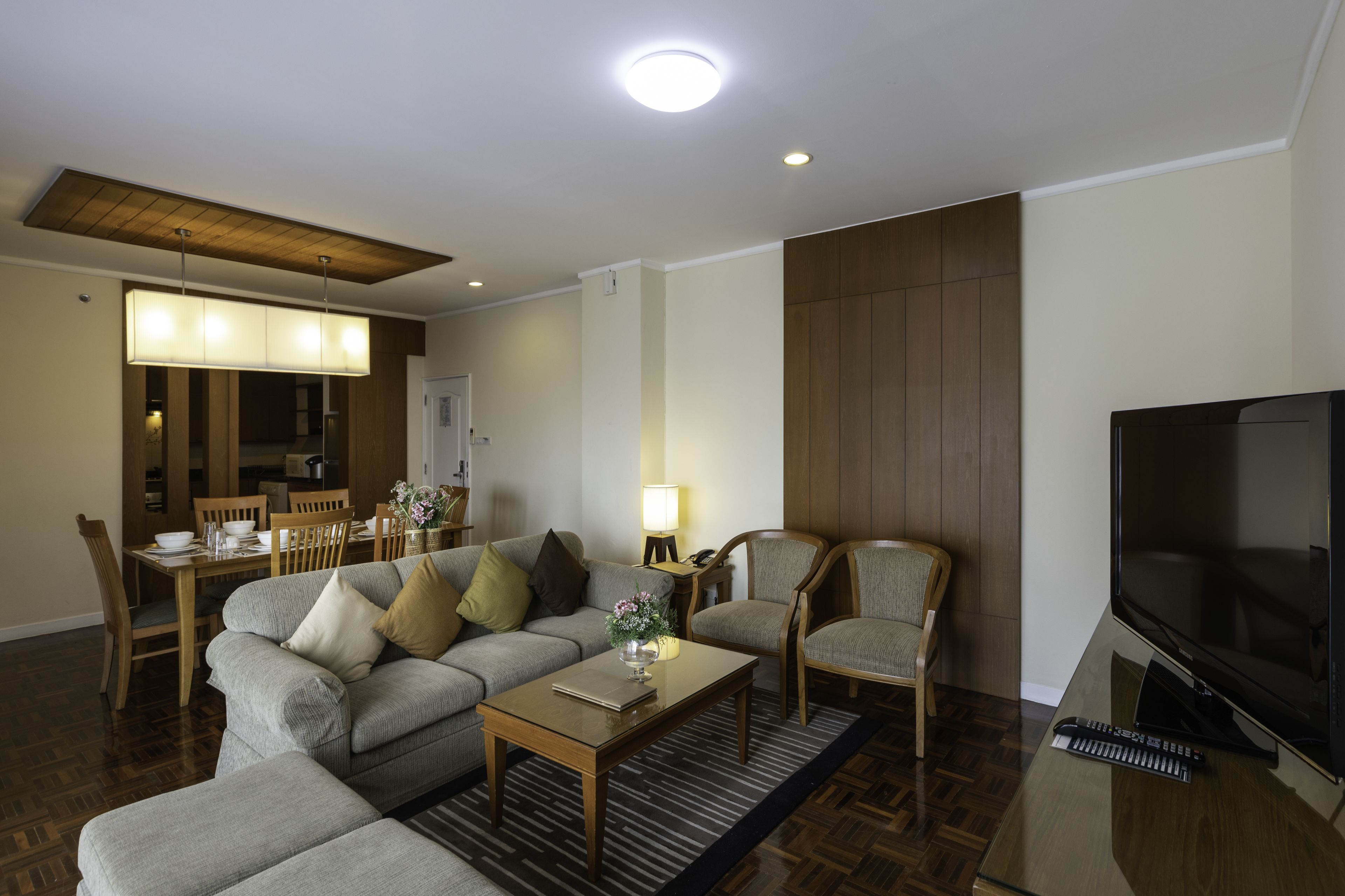 A modern living room with a sofa, chairs, a coffee table, a TV, and a dining area with a table and chairs.