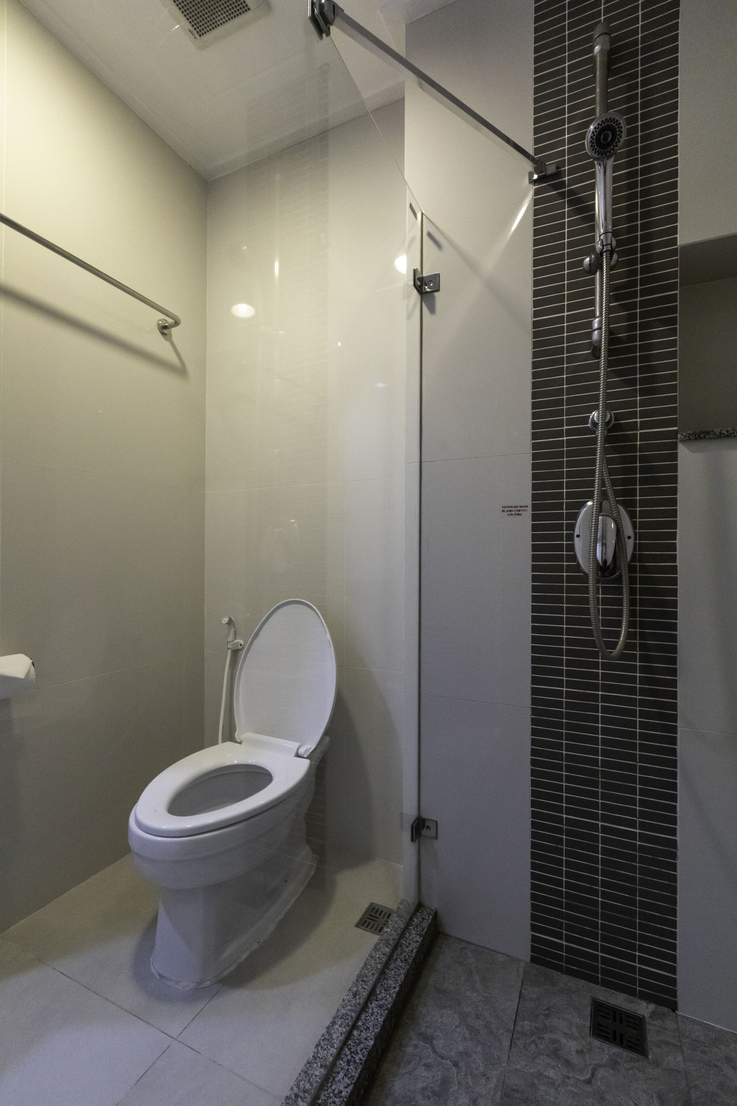 A modern bathroom with a toilet, a shower with a rain showerhead, and a tiled wall.