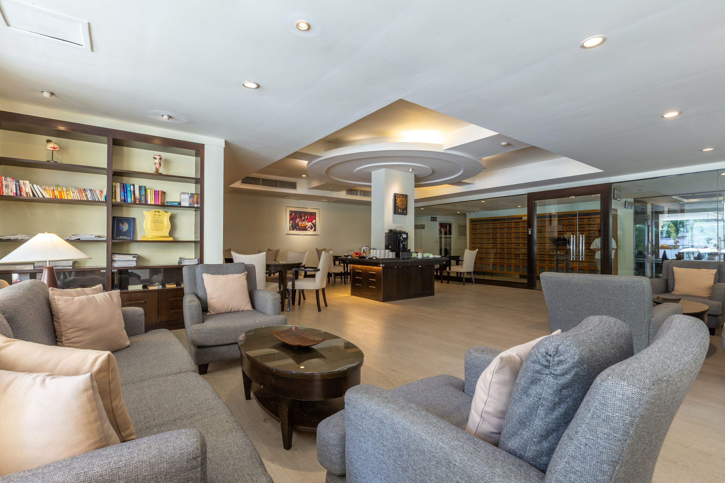 A spacious lobby with grey sofas, a coffee table, a bookshelf, and a dining area.