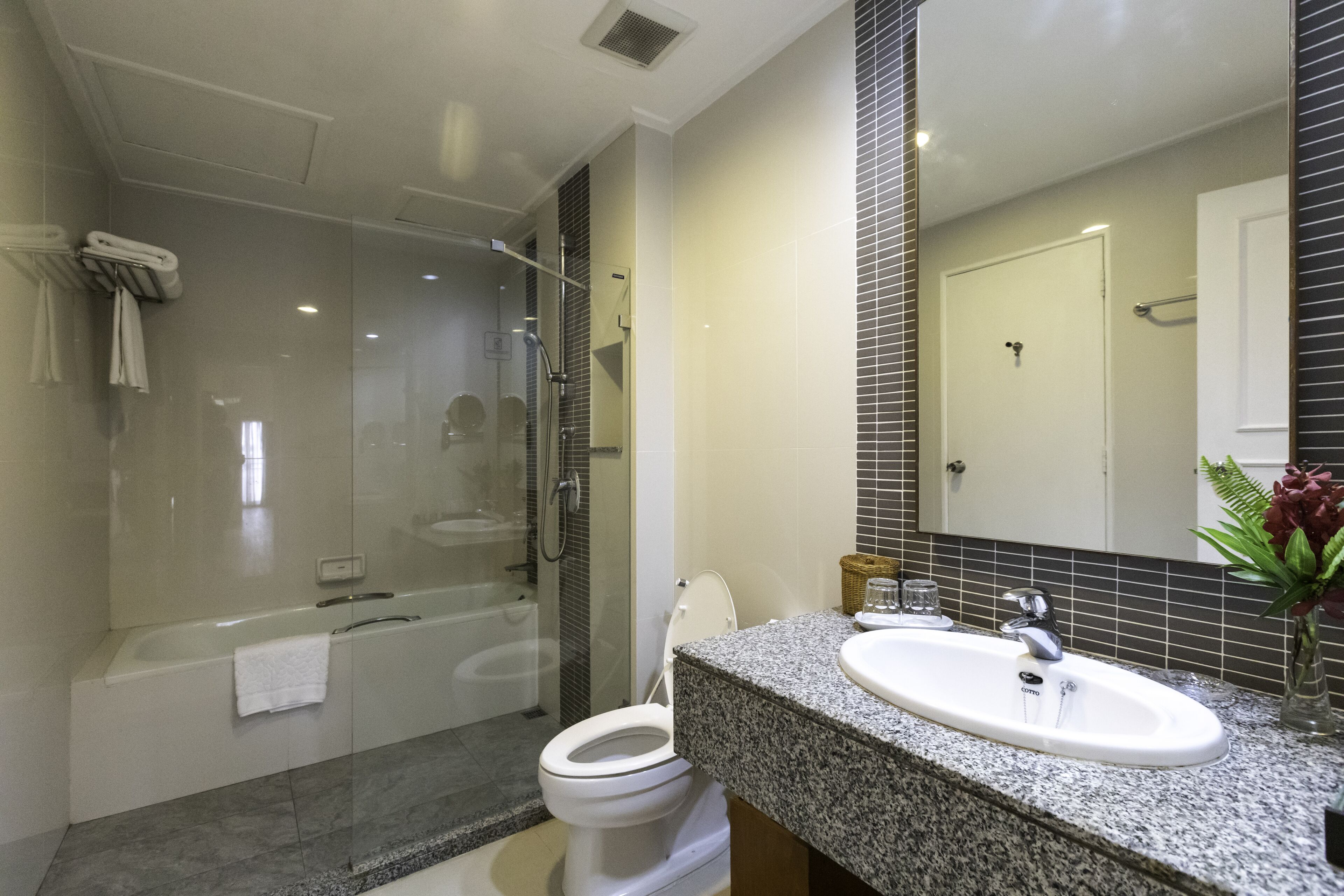 A modern bathroom with a glass-enclosed shower, a white toilet, and a granite countertop sink.