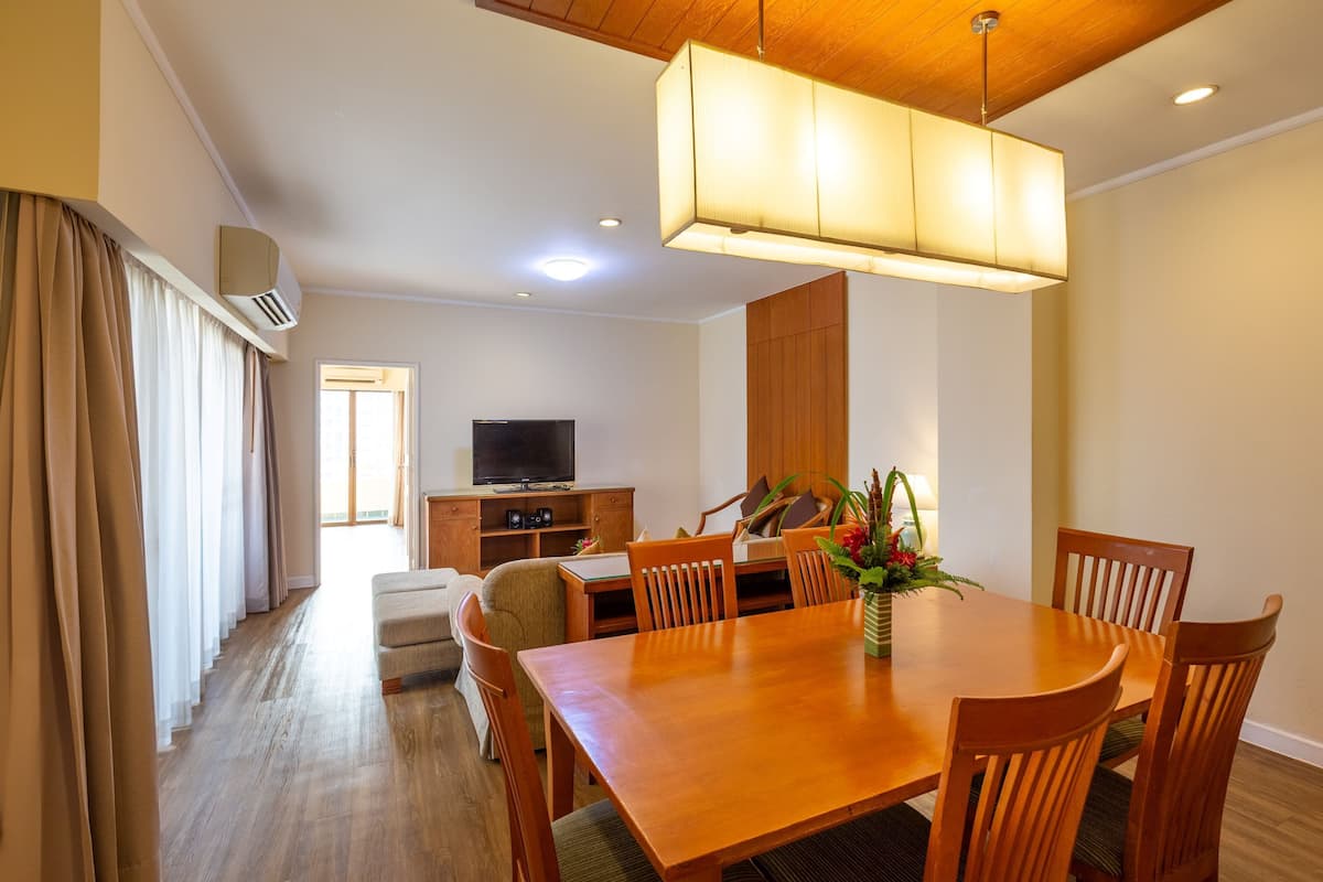 A modern dining area with a wooden table and chairs, a television in the background, and a large pendant light.