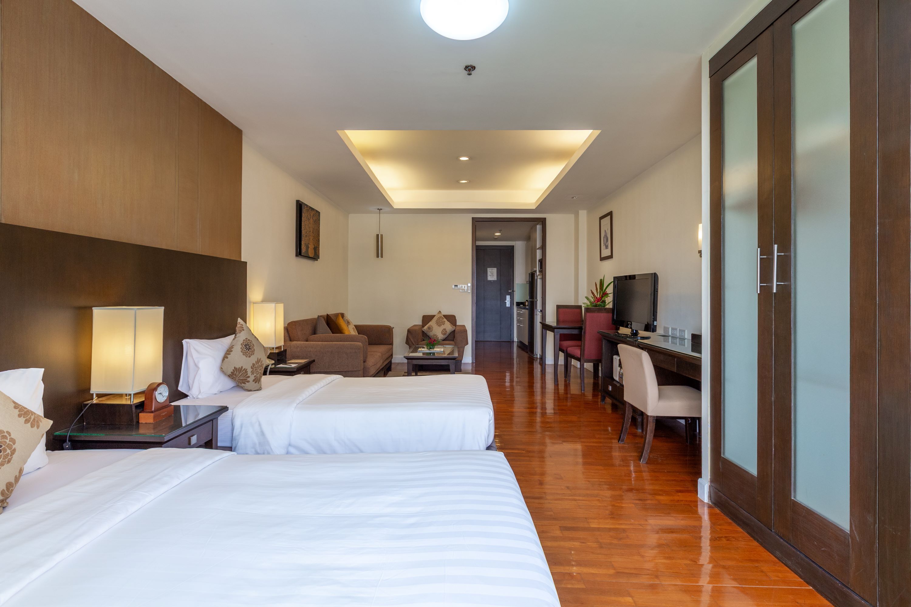 A hotel room with two beds, a desk, a TV, and a dining area.