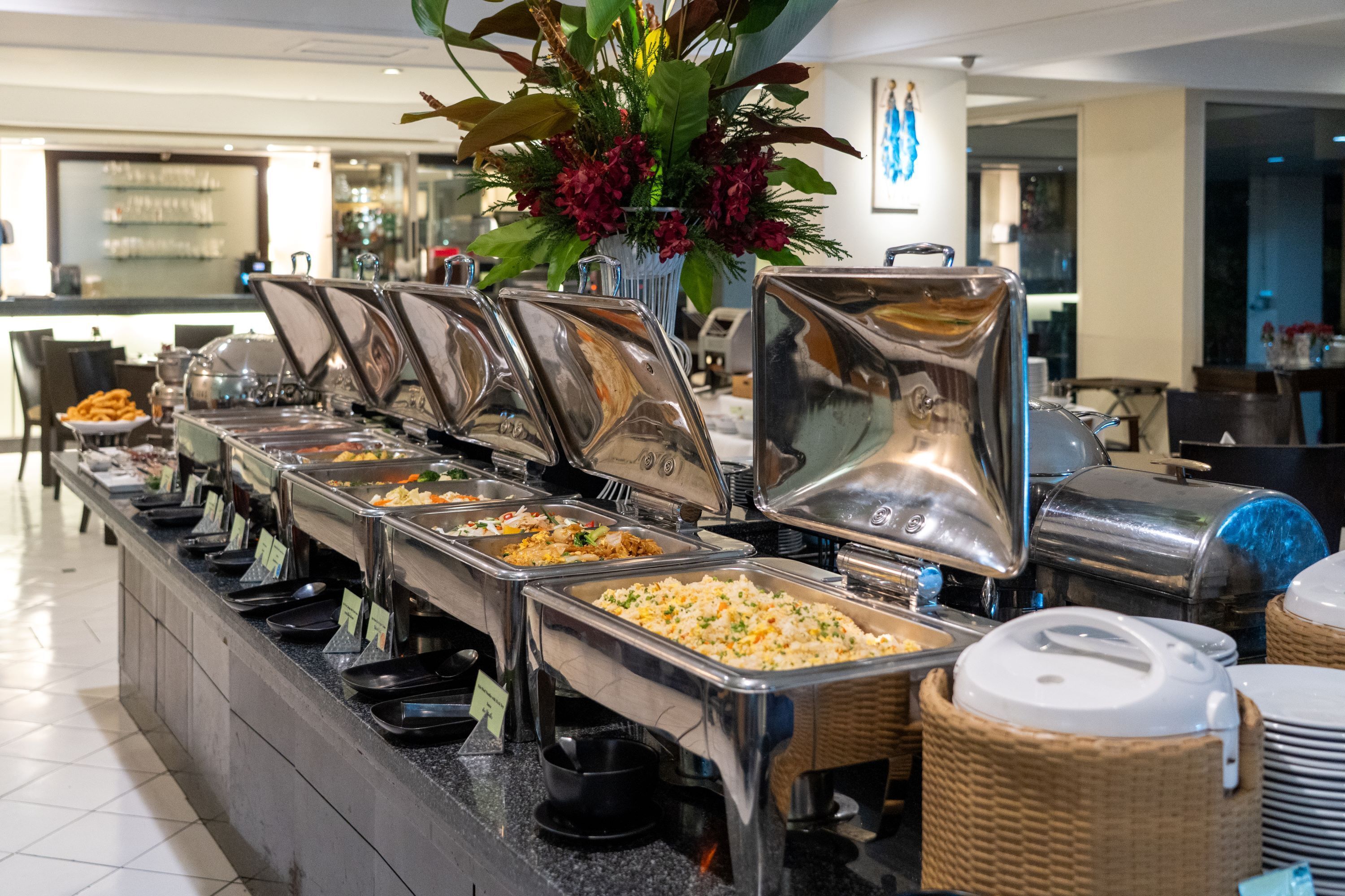 A buffet line with various food options, a decorative plant, and a glimpse of the bar area in the background.
