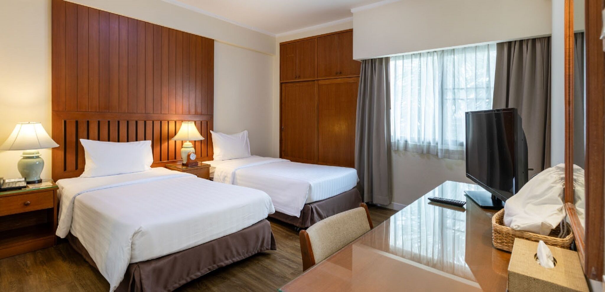 A hotel room with two beds, a desk, a television, and a window with curtains.