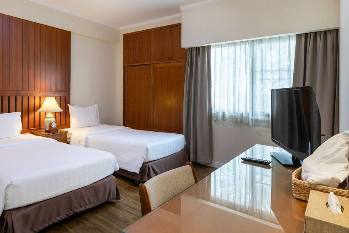 A hotel room with two beds, a desk, a television, and a window with curtains.