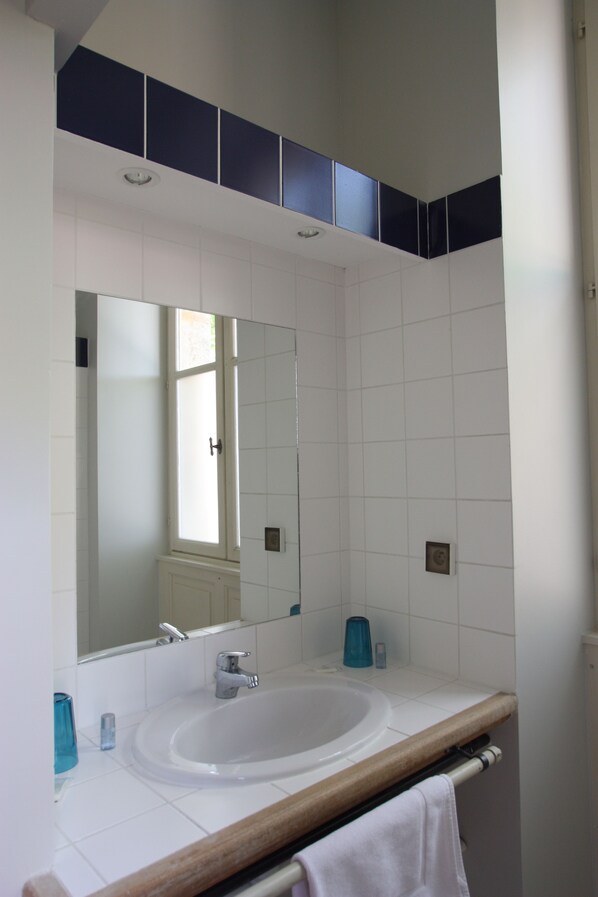 Un baño con un lavamanos blanco, un espejo y una ventana.