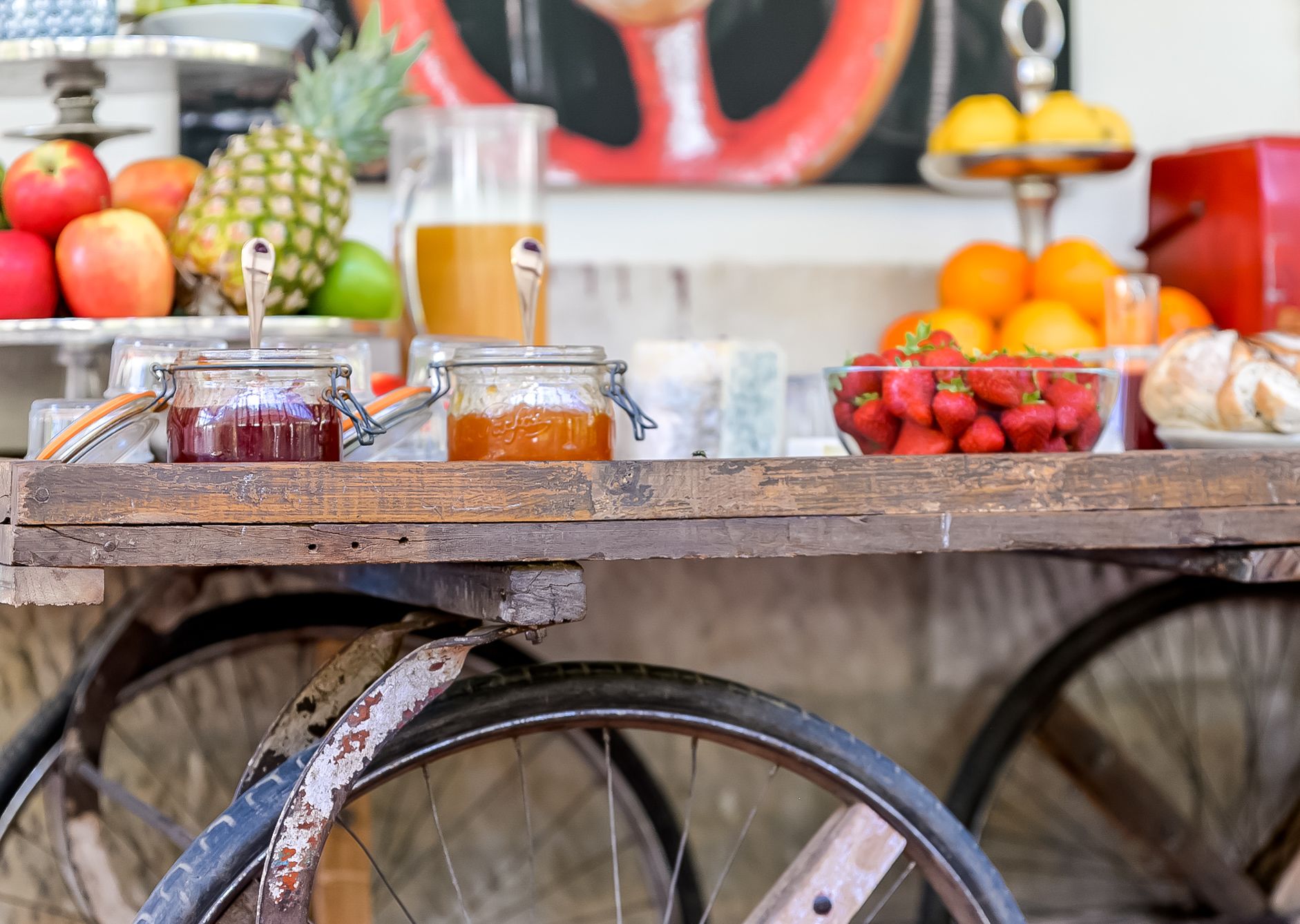 A wooden table with jars of preserves, fresh fruits, and a glass pitcher.