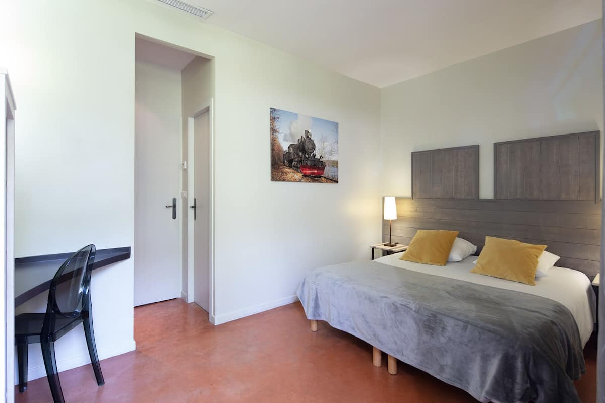 A bedroom with a bed, bedside tables, a chair, a painting, and a door.