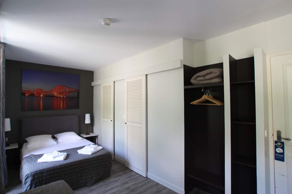 A hotel room with a bed, bedside tables, a wardrobe, and a painting on the wall.