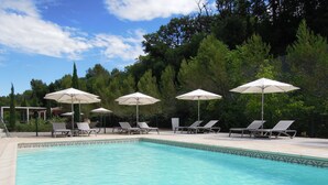 A swimming pool with lounge chairs and umbrellas, surrounded by trees. - Hotel Estelou (Sommieres)