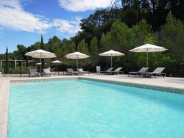 Piscina com espreguiçadeiras e guarda-sóis, cercada por árvores.