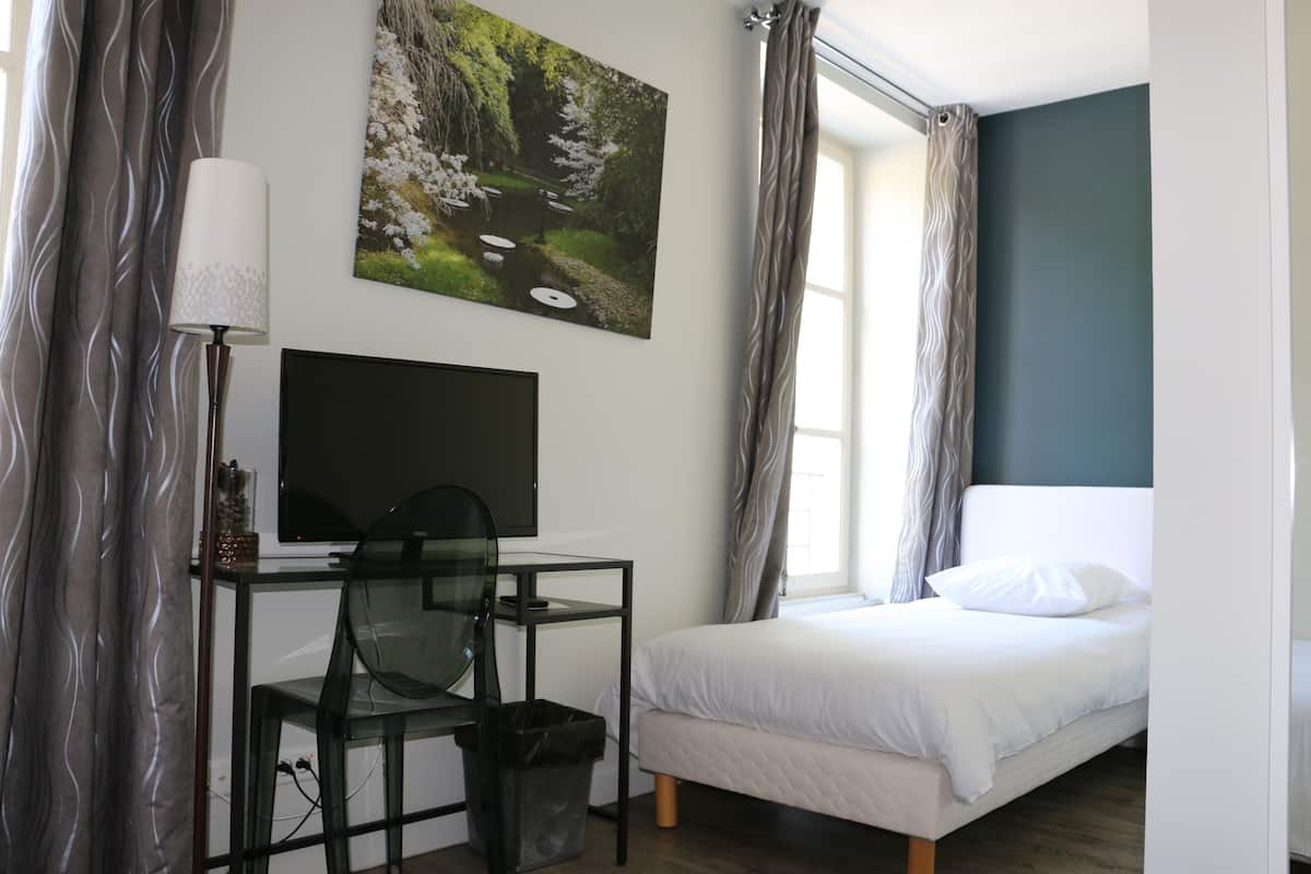 A bedroom with a bed, a desk with a chair, a TV, and a painting of a landscape.