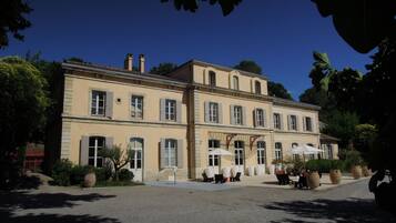 Un grand bâtiment à deux étages, doté d’une façade symétrique, de nombreuses fenêtres et d’espaces de détente en plein air agrémentés de parasols.