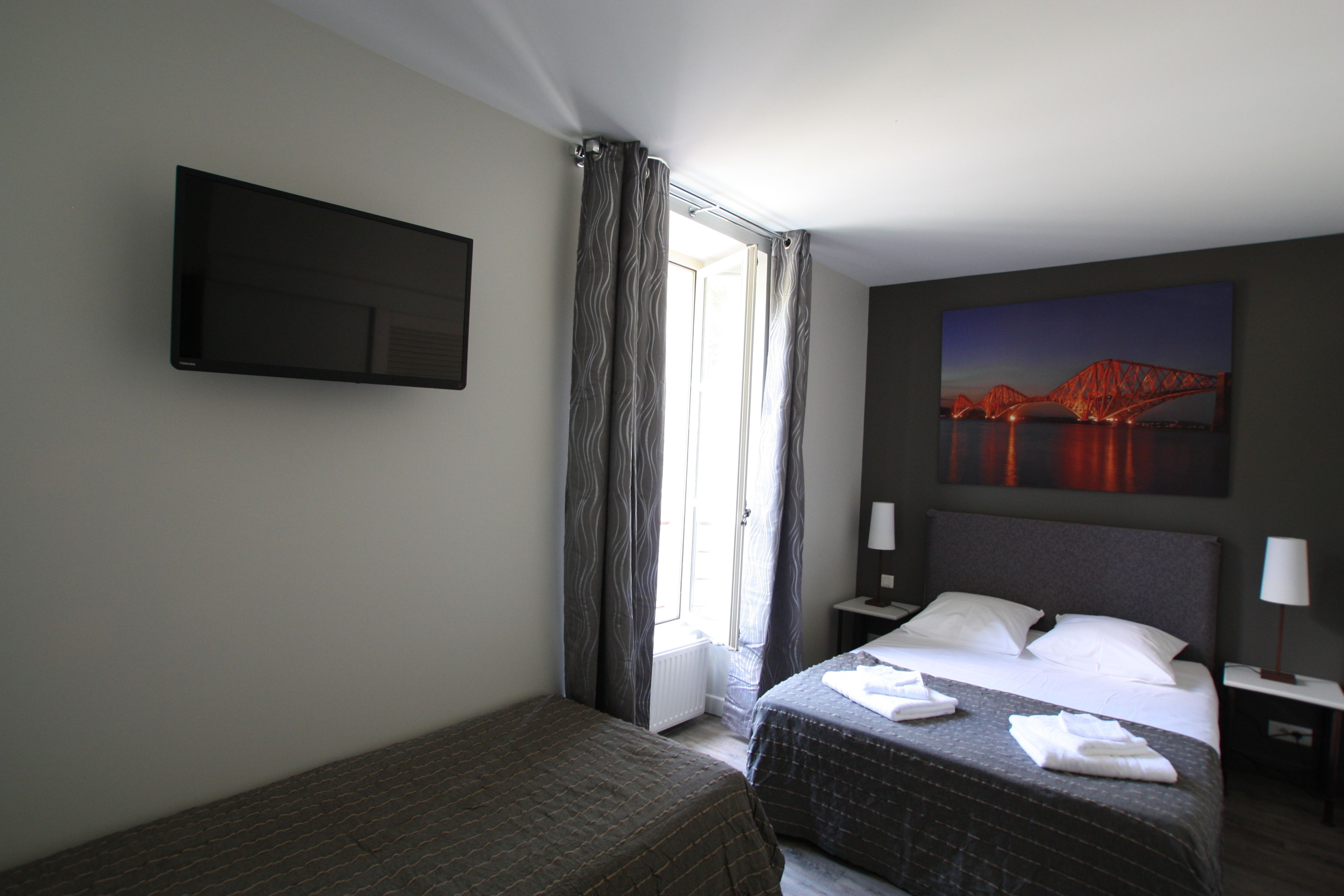 Habitación de hotel con cama, televisión de pantalla plana, un cuadro de un puente y una ventana con cortinas.