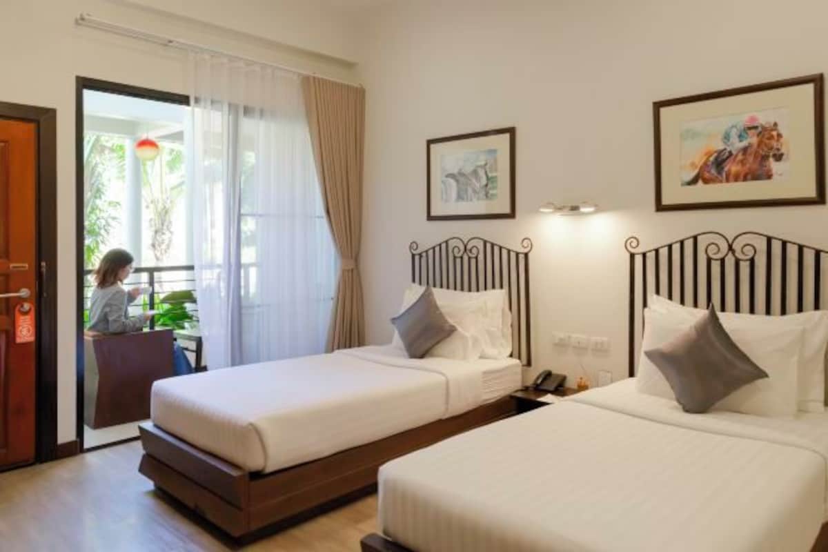 A hotel room with two beds, a sliding glass door leading to a balcony, and artwork on the walls.