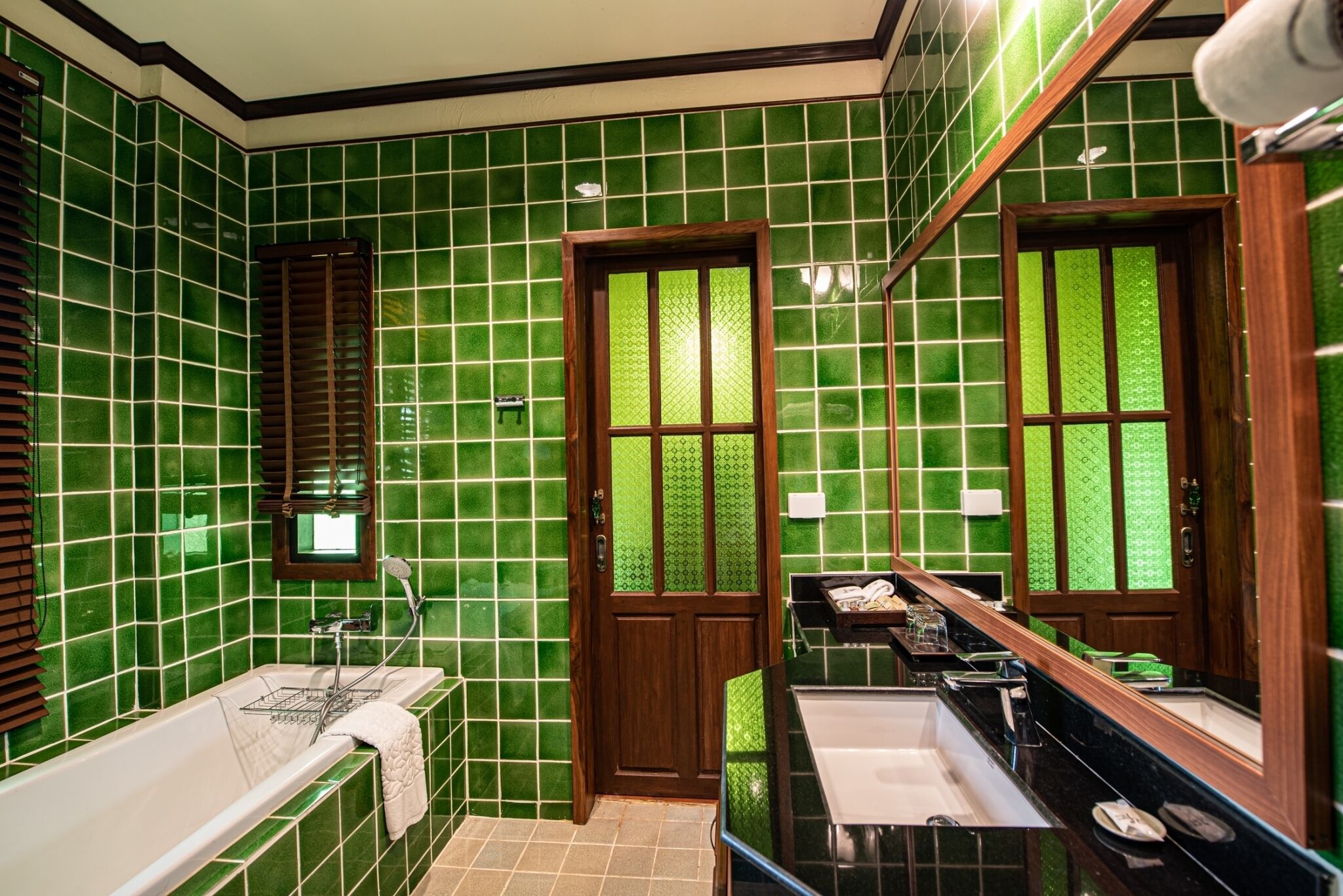 Un baño con paredes de azulejos verdes, una puerta de madera, una bañera, un lavabo y un espejo grande.