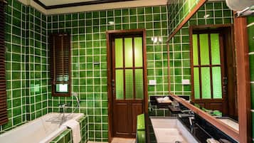 Un baño con paredes de azulejos verdes, una puerta de madera, una bañera, un lavabo y un espejo grande.