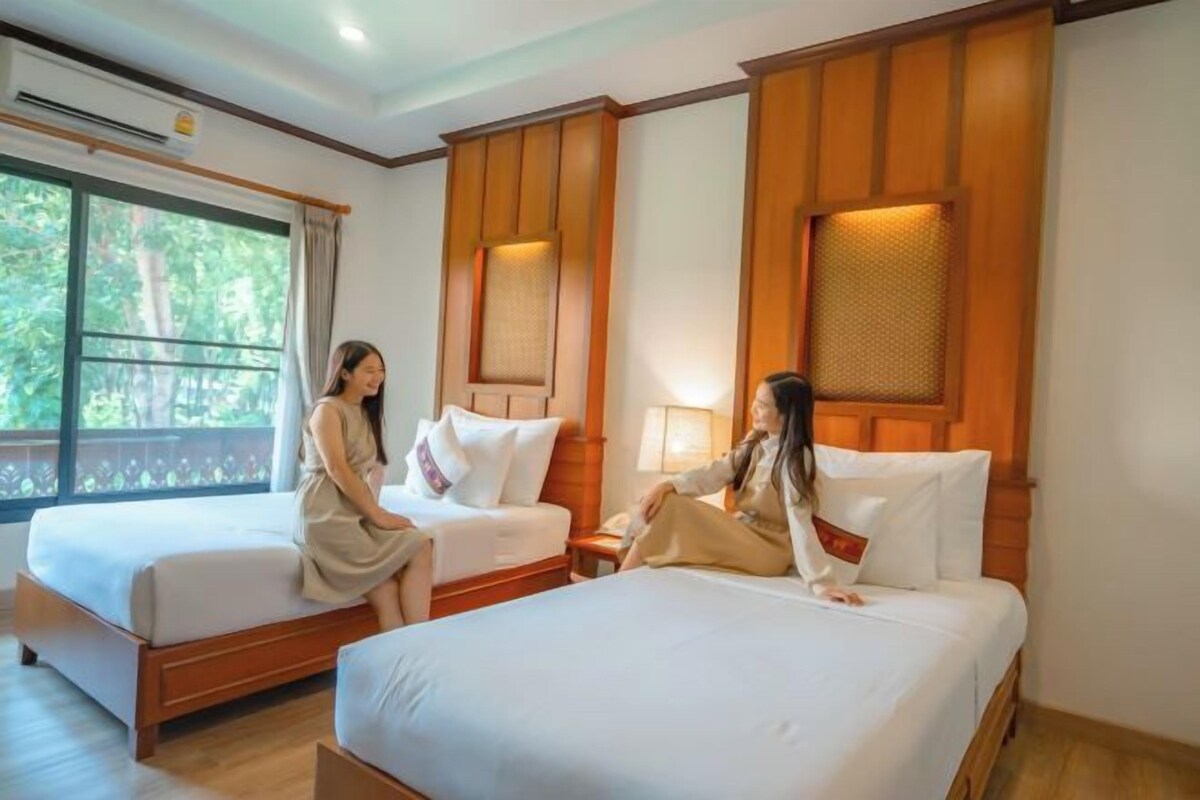 Une chambre d’hôtel avec deux lits, des têtes de lit en bois et une grande fenêtre donnant sur un paysage verdoyant.