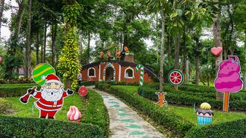 Um caminho no jardim leva a um edifício com chaminé, cercado por vegetação e diversos detalhes decorativos.