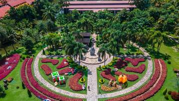 A landscaped garden with a central fountain, surrounded by palm trees and flower beds.
