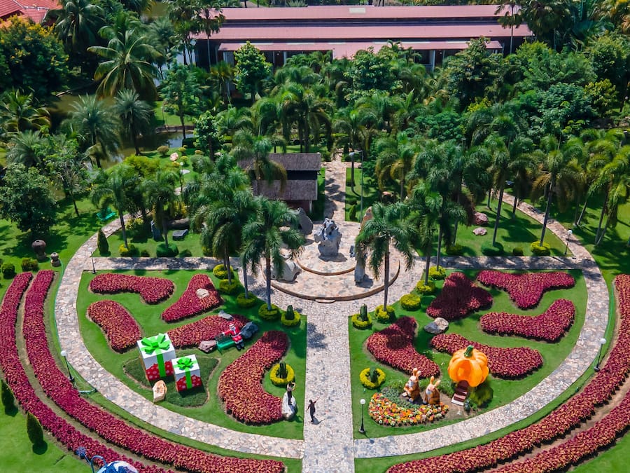 A landscaped garden with a central fountain, surrounded by palm trees and flower beds.