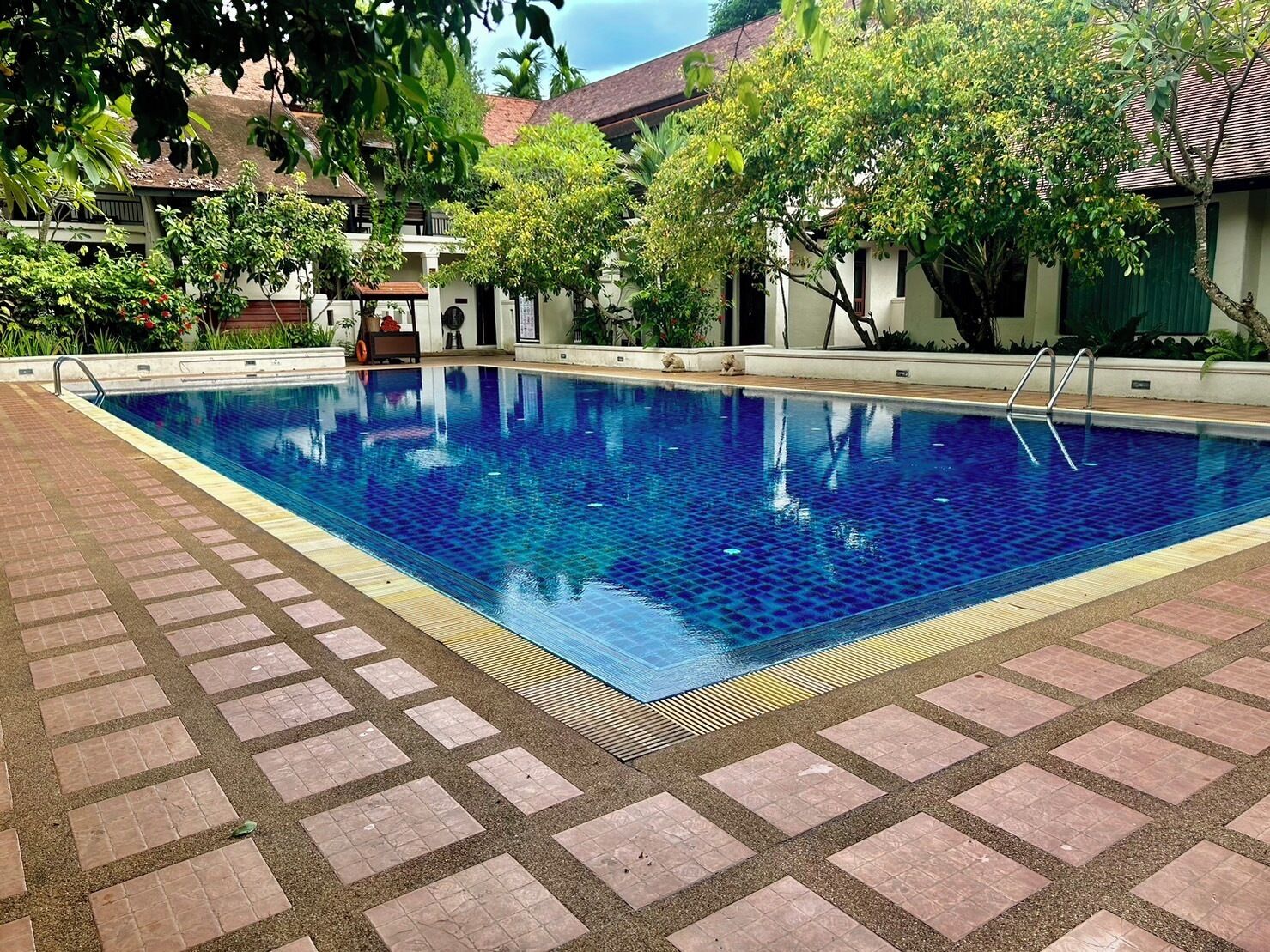 Ein rechteckiger Swimmingpool mit einer gefliesten Kante, umgeben von einem Pflasterweg.