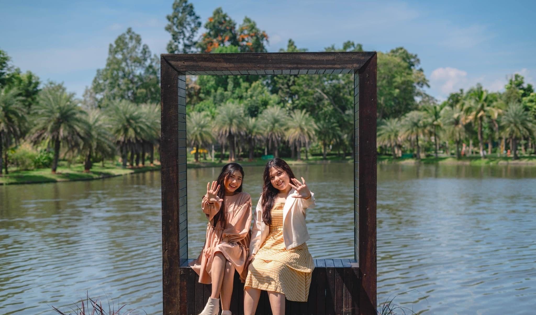 Two individuals sitting on a wooden platform by a lake, framed by a dark structure.