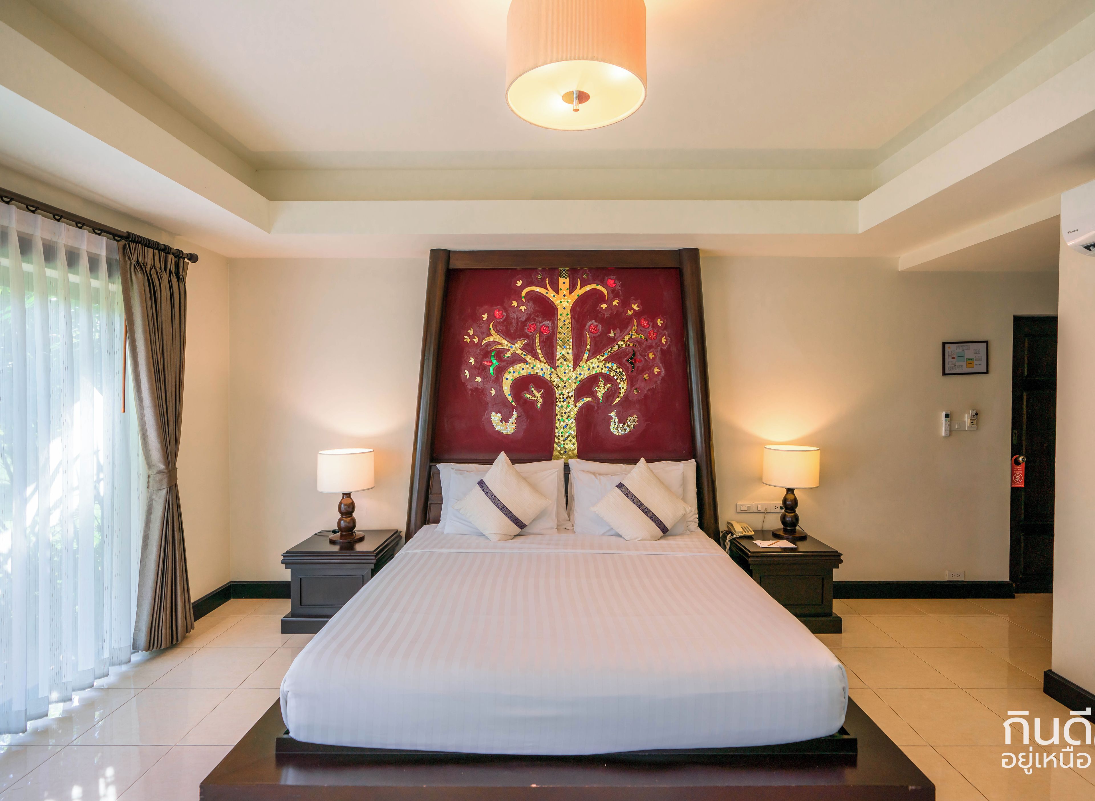 Habitación de hotel con una cama grande, dos mesitas de noche con lámparas, un cabecero decorativo y vistas al exterior a través de cortinas traslúcidas.