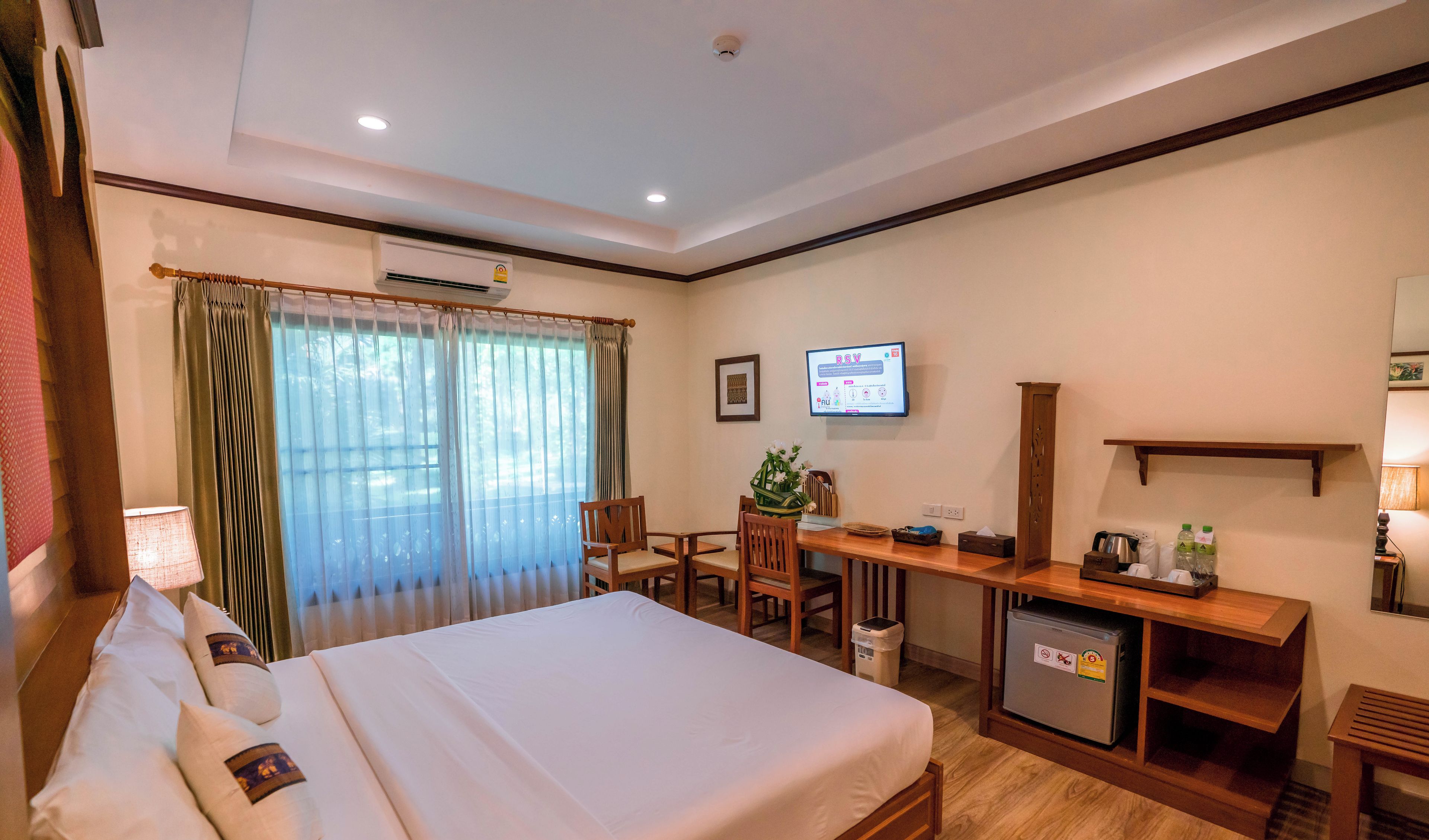 A hotel room with a bed, desk, chair, TV, and a small refrigerator.