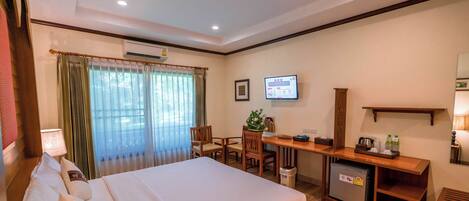 A hotel room with a bed, desk, chair, TV, and a small refrigerator.