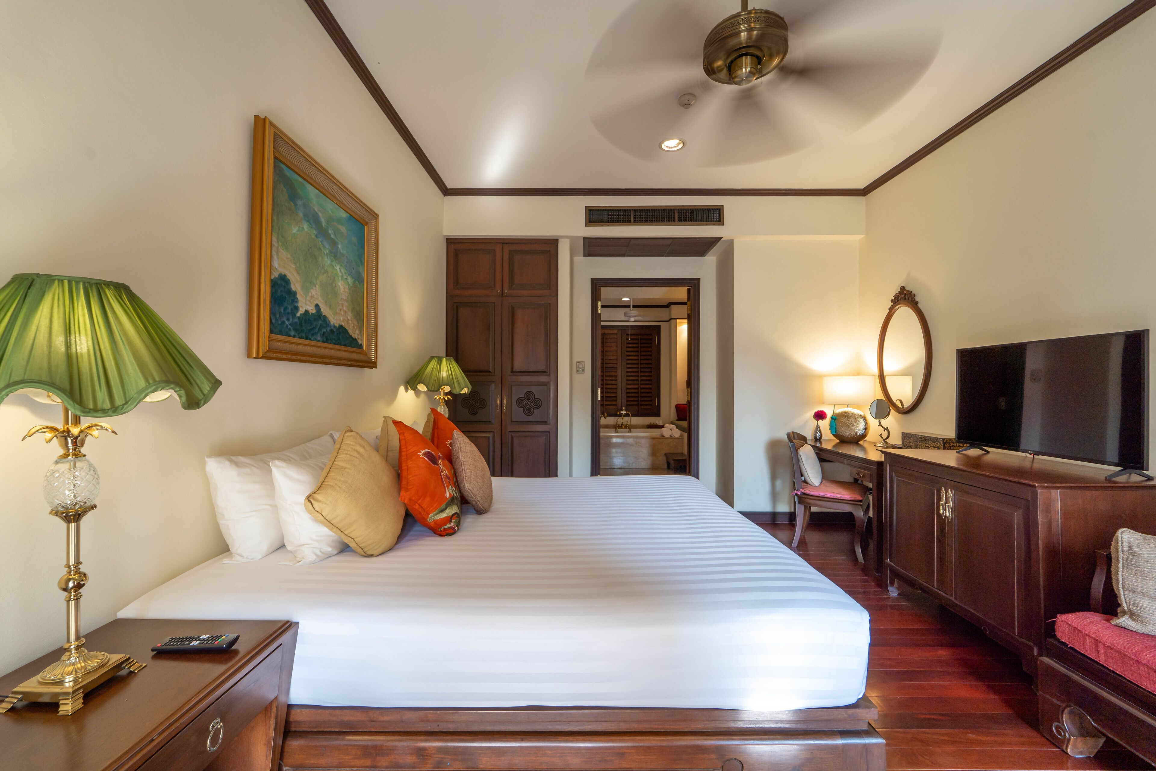 A hotel room with a large bed, a desk with a lamp, a television, and a wardrobe.