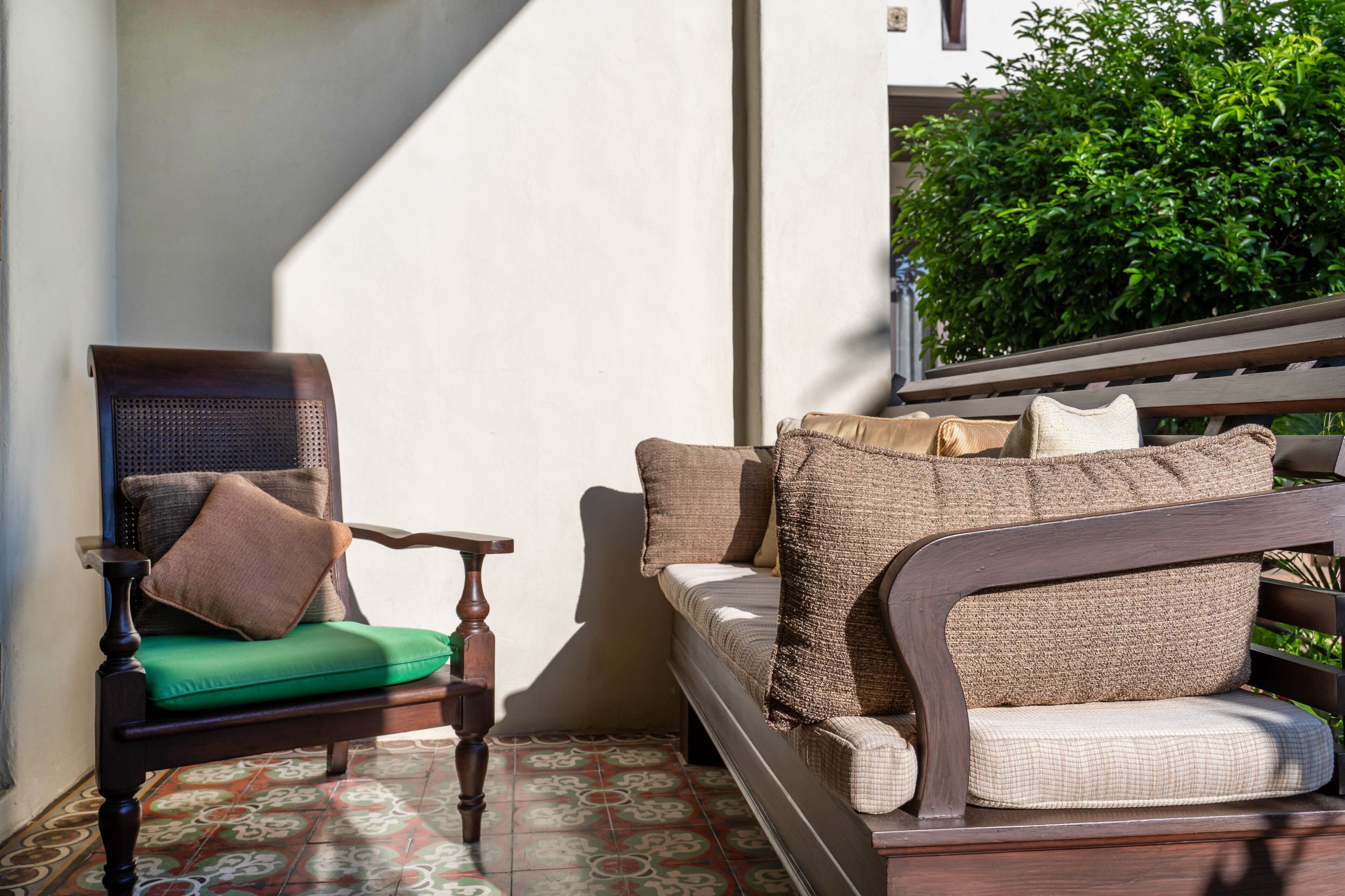 A wooden chair with a green cushion and a wicker sofa with multiple cushions.